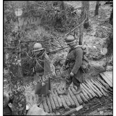 Des soldats marchent en colonne sur le sentier boueux d'une forêt dans le secteur de la 3e armée.