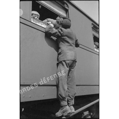 Un homme, accroché à la fenêtre d'un wagon, embrasse une femme embarquée à bord du train.