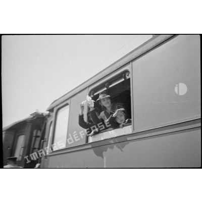 A la fenêtre d'un wagon des évacués saluent de la main en signe de départ.