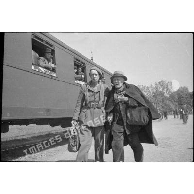 En gare de Thionville un soldat de la 3e armée guide une personne âgée pour qu'elle embarque.