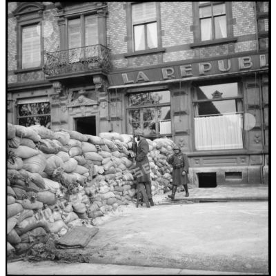 Deux soldats de la 4e armée se tiennent postés derrière un mur de sacs de sable dans une rue de Sarreguemines