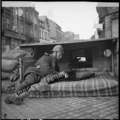 Un soldat de la 4e armée se tient posté derrière des sacs de sable dans une rue de Sarreguemines.
