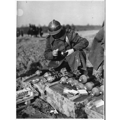 Un soldat de la 4e armée manipule des obus de mortier de 81 mm qui sont rangés au sol devant lui.