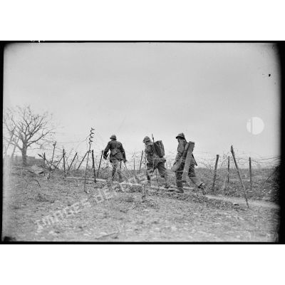Deux soldats accompagnent un officier de la 4e armée au milieu d'un réseau de barbelés.