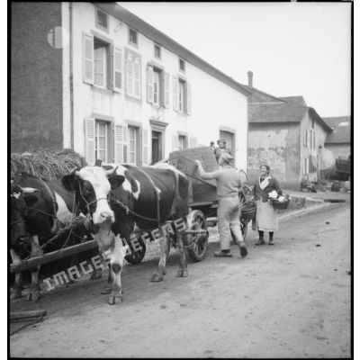 Des soldats de la 4e armée aident des civils à charger une charrette dans une rue d'un village.