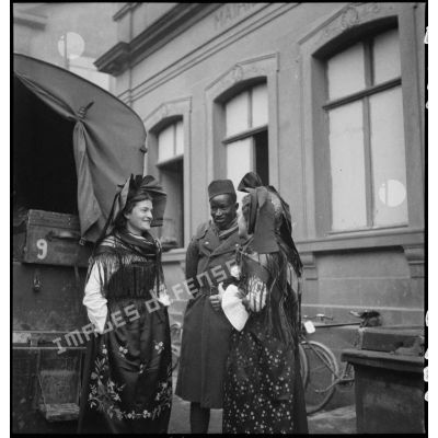 Un tirailleur sénégalais de la 5e armée est photographié entouré de deux alsaciennes en tenue traditionnelle.