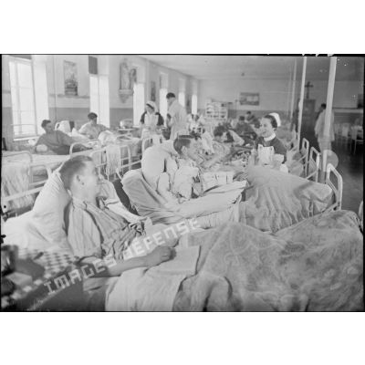 Dans la salle commune d'un hôpital militaire une infirmière britannique discute avec des blessés et des malades.