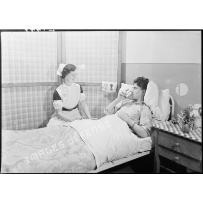 Dans une chambre d'un hôpital militaire une infirmière britannique de la Formation Hadfield Spears discute avec un blessé.