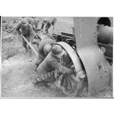 Des servants de la 5e armée poussent sur les roues d'une pièce de 155 mm court M1915/17.