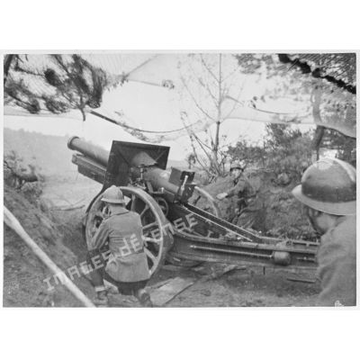 Tir d'une pièce de 155 mm court M1915/17. Cette dernière est photographiée en plan général de trois quarts dos.