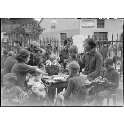 A l'extérieur dans une cour d'école, des femmes et des enfants mangent à table.
