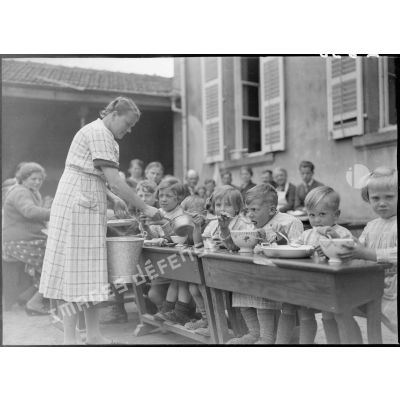 A l'extérieur dans une cour d'école, des enfants réfugiés mangent à table.