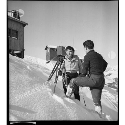 Un caméraman du SCA discute avec un lieutenant du 199e BCHM près de sa caméra posée sur trépied dans la neige.