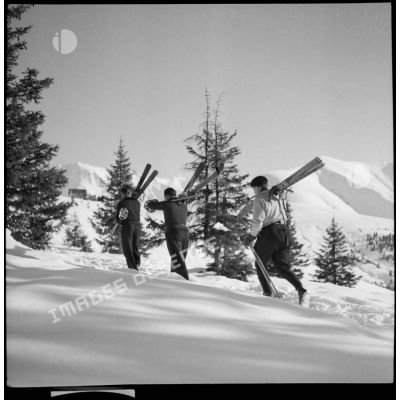 Des chasseurs du 199e BCHM, skis sur une épaule, marchent dans la neige.