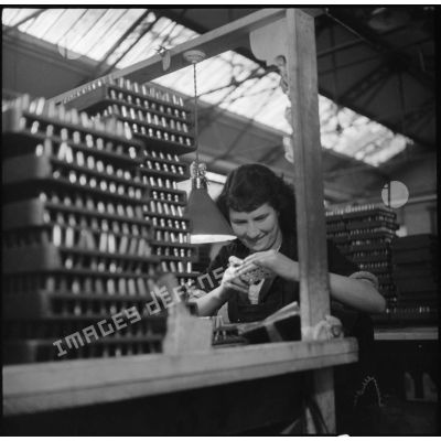 Dans l'usine, portrait d'une ouvrière qui vérifie la taille et le calibre des cartouches en fin de chaîne.