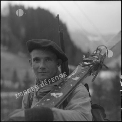 Portrait d'un chasseur alpin du 199 BCHM en tenue d'éclaireur-skieur, une paire de skis sur une épaule.