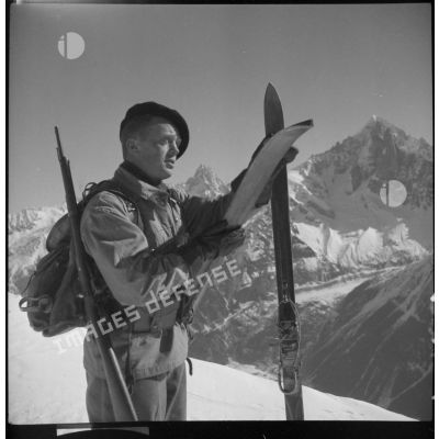 Portrait d'un chasseur alpin du 199 BCHM en tenue d'éclaireur-skieur, une paire de skis dans les mains.