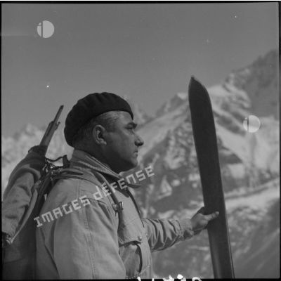 Portrait d'un chasseur alpin du 199 BCHM en tenue d'éclaireur-skieur, une paire de skis à la main.