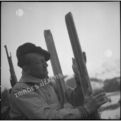 Portrait d'un chasseur alpin du 199 BCHM en tenue d'éclaireur-skieur, une paire de skis à la main.