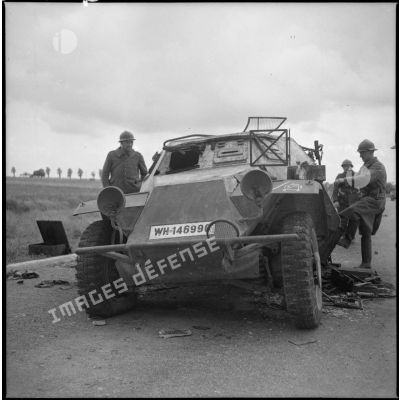 Des soldats français observent un véhicule allemand abandonné sur le bord d'une route.