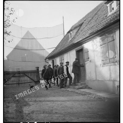 Des soldats et un douanier invités à entrer dans une maison de village par un habitant.