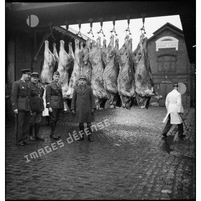 Officiers devant des carcasses de viande accroché dans la cour d'un abattoir.