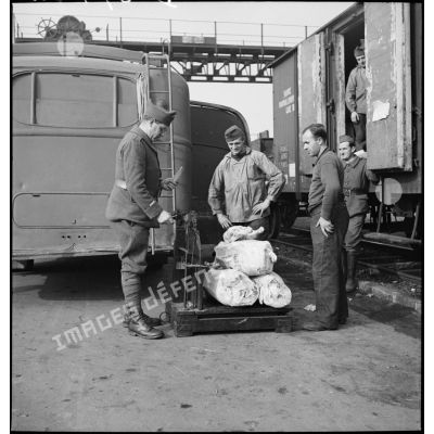 Soldat pesant des sacs contenant vraisemblablement des pièces de viande, à proximité d'un wagon.
