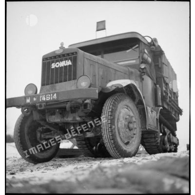 Plan rapproché d'un tracteur lourd de dépanage de chars de type Somua MCL 5 sur une route de campagne enneigée.
