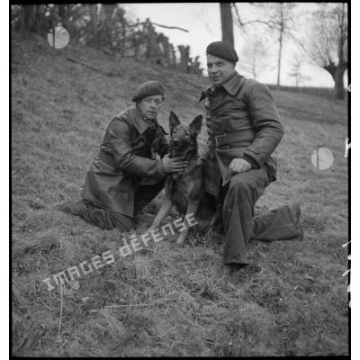 Deux soldats et leur chien, assis en marge d'une formation cynophile.