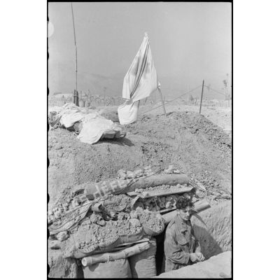 Soldat dans une tranchée à l'entrée d'une antenne chirurgicale du camp retranché de Diên Biên Phu, sur laquelle flotte le drapeau blanc à Croix-rouge.