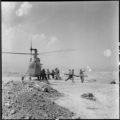 Embarquement de blessés dans un hélicoptère Sikorksy S55 au cours d'une évacuation sanitaire à Diên Biên Phu, sous le feu de l'artillerie Viêt-minh malgré les fanions à croix rouge agités par les brancardiers.