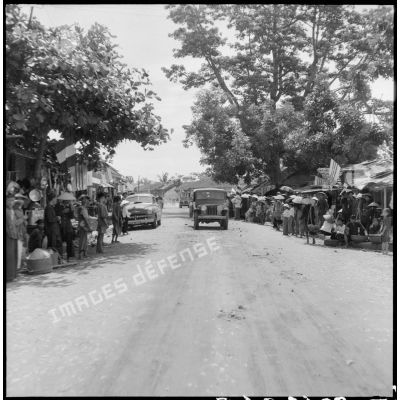 Passage du convoi de véhicules transportant les membres de la mission militaire américaine Melby-Erskine dans les rues pavoisées de Dap Cau.