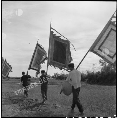 Les drapeaux des génies tutélaires des villages sont promenés le long de la route en l'honneur de la commission américaine Melby-Erskine en visite au Tonkin.