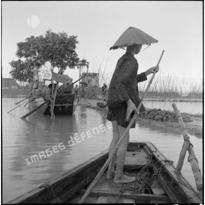 Passage de matériel sur des barques pour construire une diguette contre l'inondation à l'entrée d'un poste militaire.