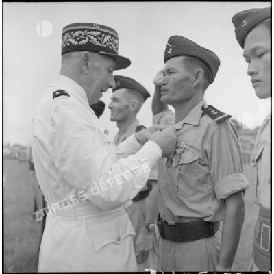 Remise de décoration à un sous-lieutenant du bataillon de marche indochinois (BMI) par le général Marchand au cours d'une cérémonie sur le stade d'Haïduong.