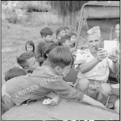 Distribution de documents aux enfants de la communauté catholique de Yen Vi par des militaires se déplaçant à bord d'une jeep.