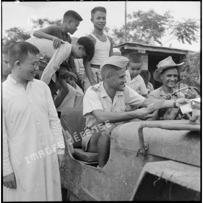Distribution de documents aux enfants de la communauté catholique de Yen Vi par des militaires se déplaçant à bord d'une jeep.