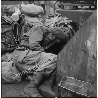 Un commando marine dort au milieu des paquetages sur le pont d'un LCI (landing craft infantry) pendant la traversée de la baie d'Along.