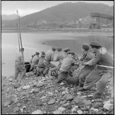 Des commandos marine hissent une embarcation sur le rivage de pierres.