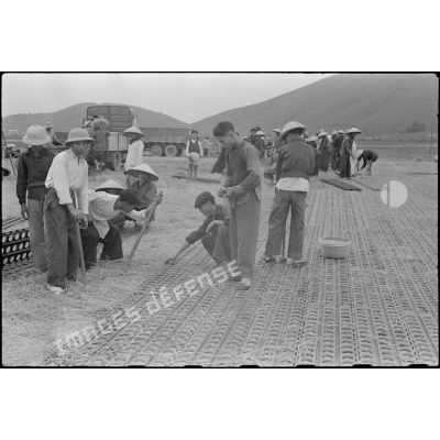 Des travailleurs tonkinois posent des plaques d'acier perforées (PSP) pour l'aménagement de la piste du terrain d'aviation de Kien An.