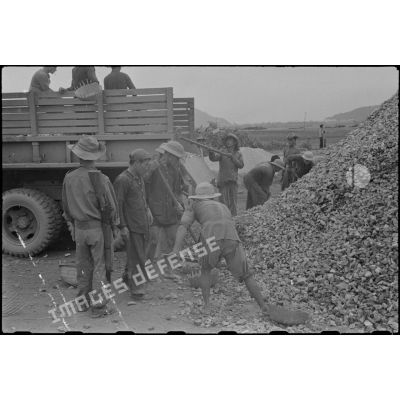 Des travailleurs tonkinois chargent des gravats à bord d'un camion GMC au cours des travaux d'aménagement du terrain d'aviation à Kien An.