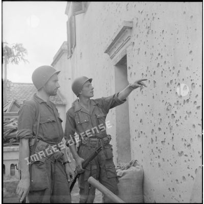 Deux légionnaires du 2e BEP regardent des impacts de balles sur le mur d'une maison.