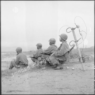 Des soldats vietnamiens, assis au bord de la route, armés de fusils MAS 36.