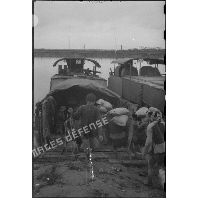 Des prisonniers du Viêt-minh chargent des sacs de riz dans des LCM (landing craft medium.