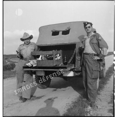 Moment de détente pour deux soldats qui boivent une bouteille à l'arrière d'un véhicule léger stoppé sur une route du Tonkin.