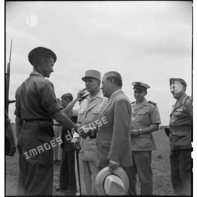 Le général de Lattre de Tassigny, commandant en chef en Indochine et Tran Van Huu, président du conseil des ministre de l'Etat du Vietnam; félicitent un soldat au cours d'une prise d'armes sur le terrain d'aviation de Vinh Yen.