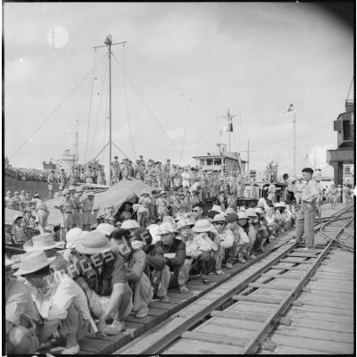 Vietnamiens attendant accroupis sur un quai du port d'Hanoi (Haiphong ?).