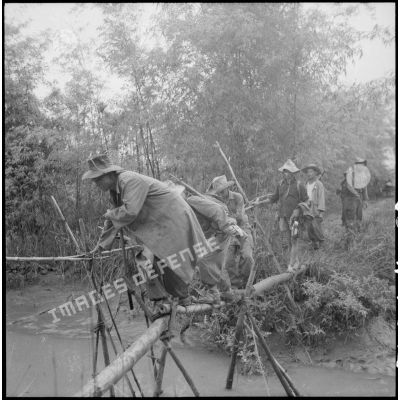 Progression des troupes françaises sur un pont de bambou.