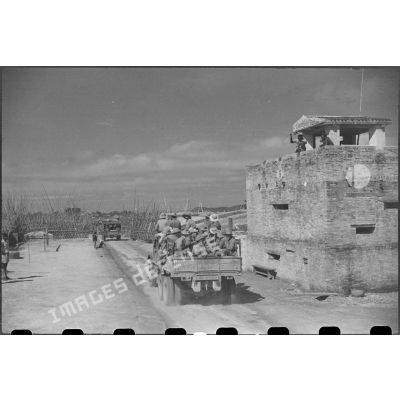 Passage des troupes en camion devant un poste fortifié.