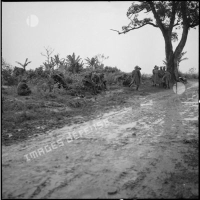 Un groupe de soldats attend sur le bord d'une route détrempée.